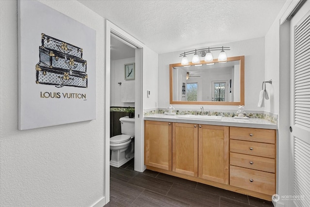 bathroom featuring vanity, ceiling fan, toilet, and a textured ceiling