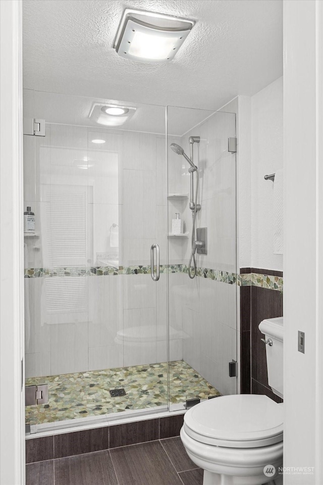 bathroom featuring a shower with shower door, a textured ceiling, and toilet