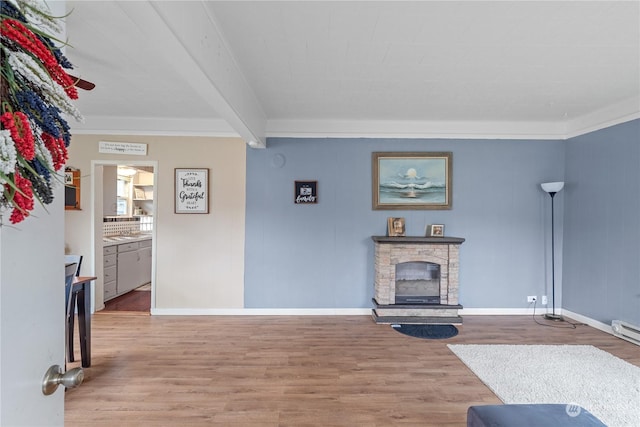 living room with beam ceiling, a stone fireplace, crown molding, and light hardwood / wood-style flooring