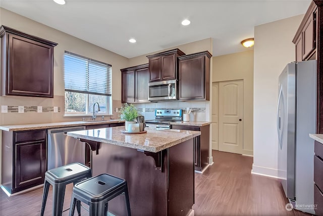 kitchen with sink, dark hardwood / wood-style floors, a kitchen island, a kitchen bar, and stainless steel appliances