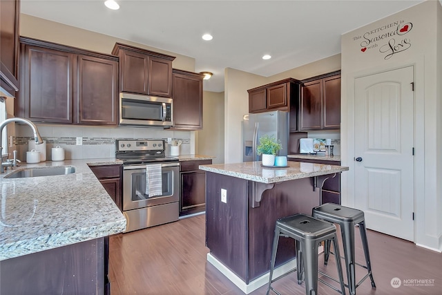 kitchen with light stone countertops, sink, a center island, a breakfast bar area, and appliances with stainless steel finishes