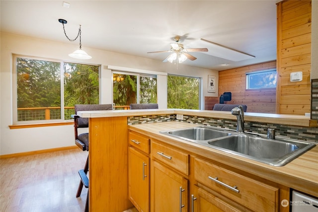 kitchen with ceiling fan, sink, hanging light fixtures, light hardwood / wood-style floors, and decorative backsplash