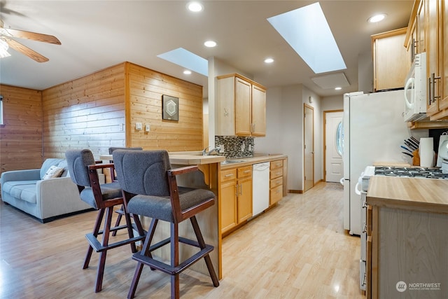 kitchen with a skylight, light hardwood / wood-style flooring, wood walls, white appliances, and light brown cabinetry