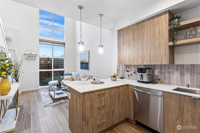 kitchen with decorative light fixtures, dishwasher, light wood-type flooring, tasteful backsplash, and kitchen peninsula