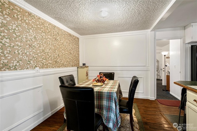 dining space featuring wallpapered walls, dark wood finished floors, wainscoting, ornamental molding, and a textured ceiling