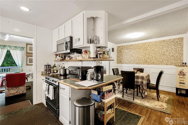 kitchen featuring dark wood-style flooring, range with electric cooktop, wainscoting, stainless steel microwave, and wallpapered walls