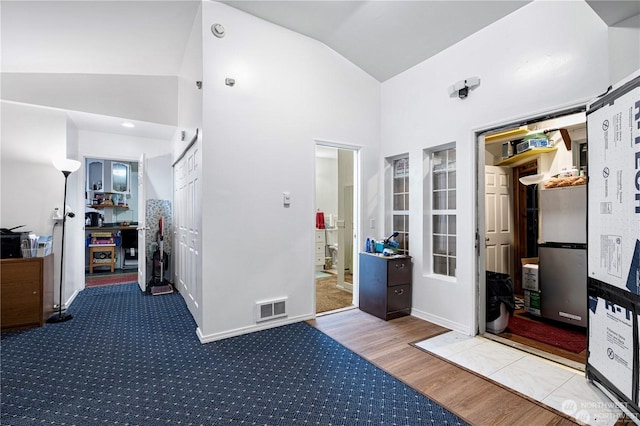 interior space featuring high vaulted ceiling, a barn door, wood finished floors, visible vents, and baseboards