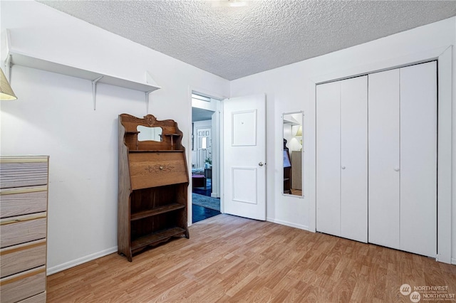 bedroom with light wood finished floors, a closet, baseboards, and a textured ceiling