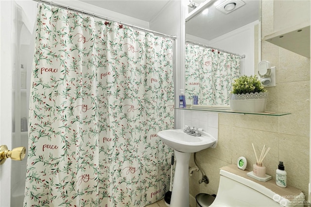 bathroom with toilet, a shower with shower curtain, a sink, and tile walls