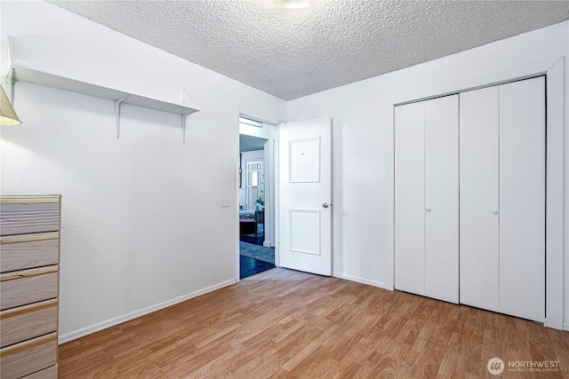 unfurnished bedroom with light wood-style flooring, a closet, baseboards, and a textured ceiling