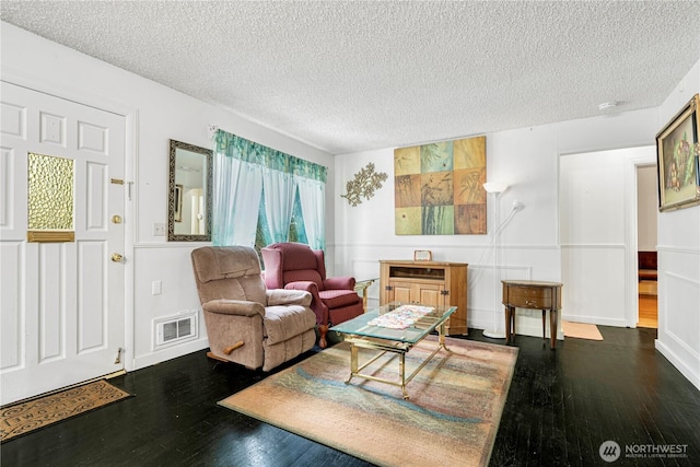 living room featuring dark wood-type flooring, visible vents, and a textured ceiling