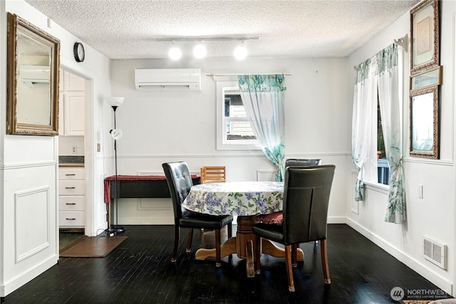 dining room with a textured ceiling, a wall unit AC, dark wood-type flooring, visible vents, and baseboards