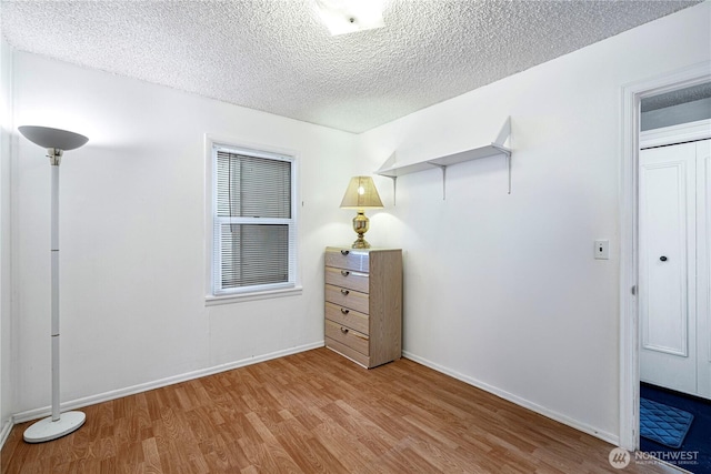 unfurnished bedroom with a textured ceiling, baseboards, and wood finished floors