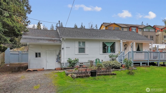 back of house with fence, a lawn, a vegetable garden, and a shingled roof
