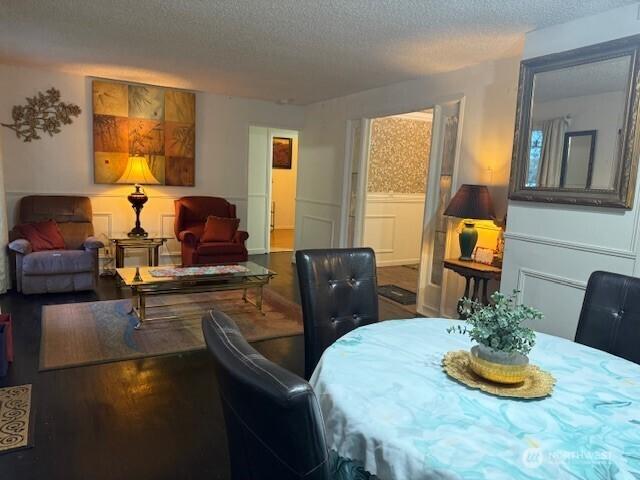 dining area with a decorative wall, wood finished floors, wainscoting, and a textured ceiling