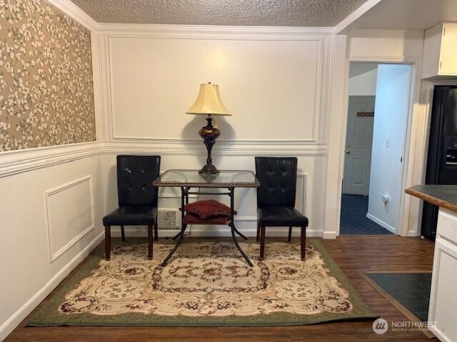 living area featuring a decorative wall, ornamental molding, a textured ceiling, and wood finished floors