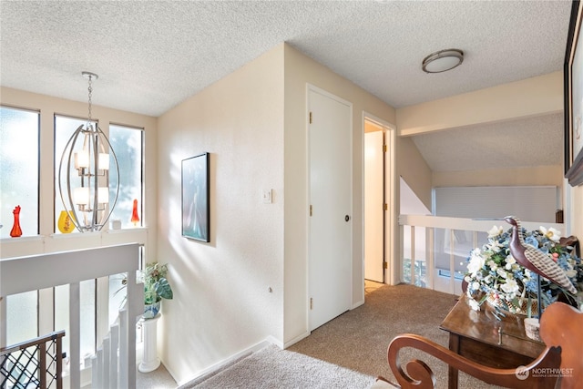 hall featuring a textured ceiling, carpet floors, and an inviting chandelier