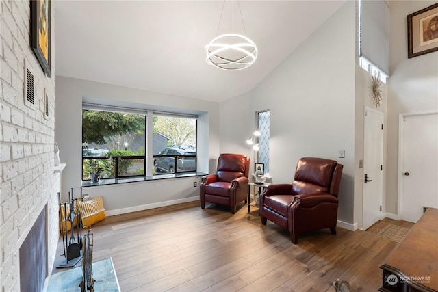 living area featuring hardwood / wood-style floors, high vaulted ceiling, and a stone fireplace