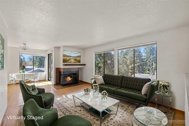 living area featuring baseboards, a fireplace with flush hearth, a textured ceiling, and wood finished floors