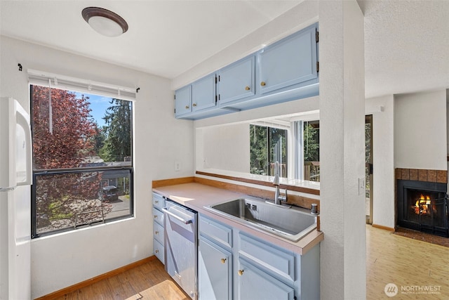 kitchen with a sink, stainless steel dishwasher, baseboards, light wood-style floors, and blue cabinetry