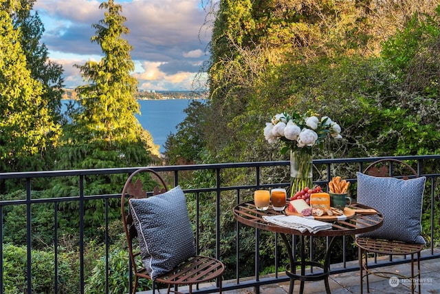 balcony at dusk featuring a water view