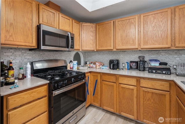 kitchen featuring stainless steel appliances, light countertops, light wood-style floors, and tasteful backsplash