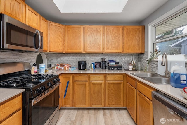 kitchen featuring light wood finished floors, stainless steel appliances, light countertops, decorative backsplash, and a sink