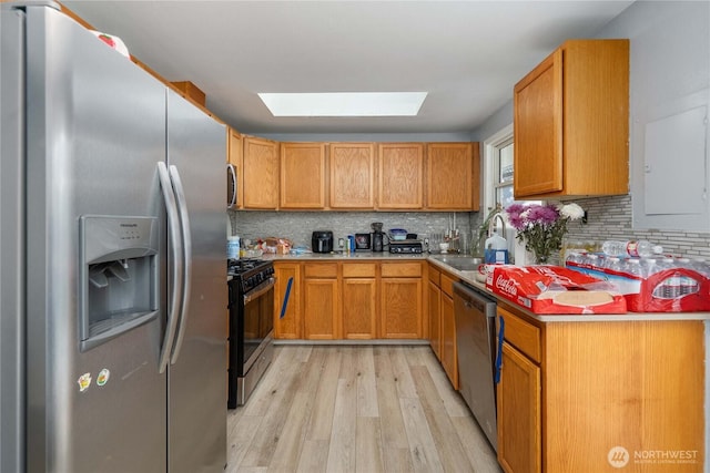 kitchen featuring a skylight, backsplash, appliances with stainless steel finishes, a sink, and light wood-type flooring