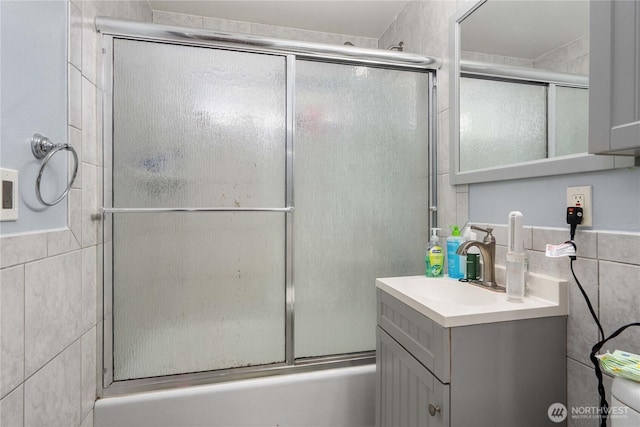 full bath with tile walls, vanity, and bath / shower combo with glass door