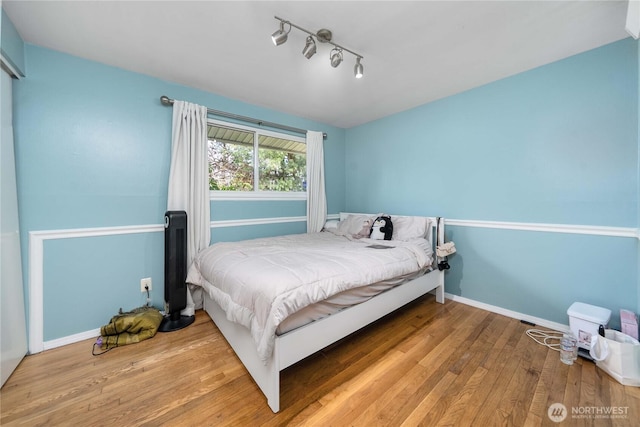 bedroom featuring wood-type flooring, rail lighting, and baseboards