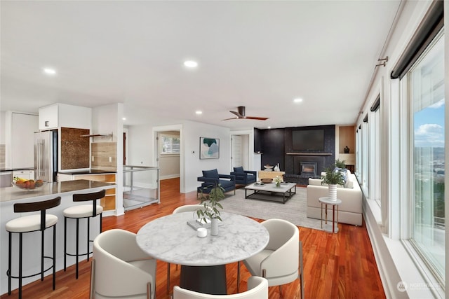 dining space featuring ceiling fan, wood-type flooring, and a brick fireplace