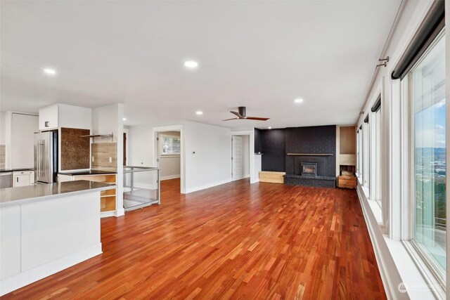 unfurnished living room featuring a brick fireplace, ceiling fan, and light wood-type flooring