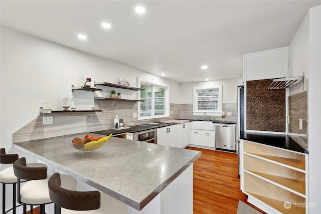 kitchen featuring a breakfast bar area, light hardwood / wood-style flooring, appliances with stainless steel finishes, white cabinetry, and kitchen peninsula