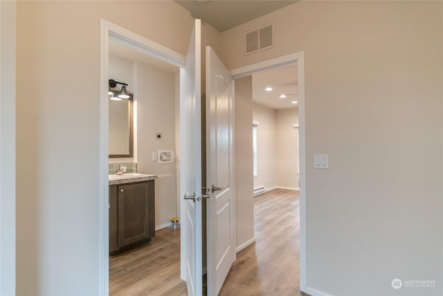 corridor with baseboard heating, sink, and light hardwood / wood-style floors