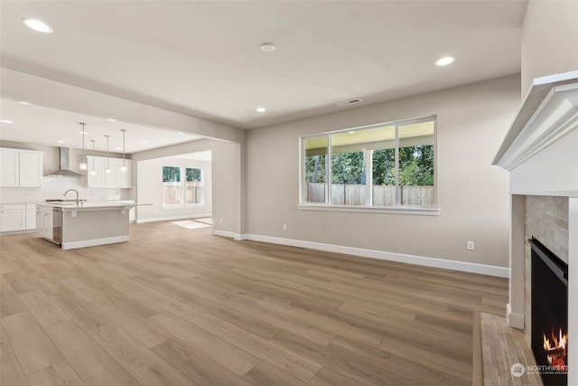 unfurnished living room with sink, light hardwood / wood-style flooring, a wealth of natural light, and a tiled fireplace