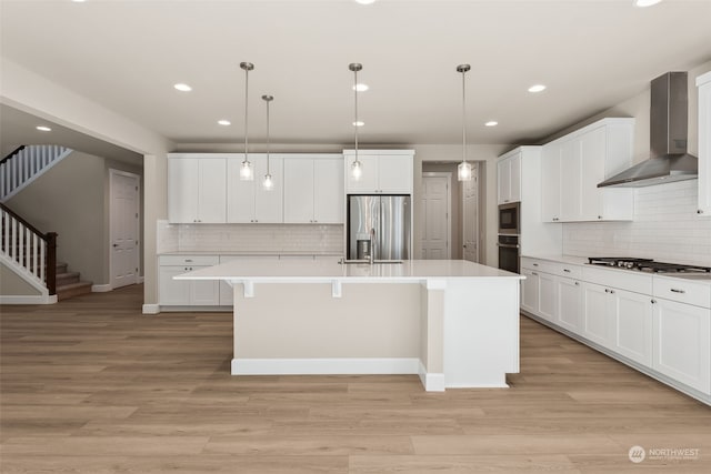 kitchen featuring a center island with sink, pendant lighting, wall chimney range hood, and appliances with stainless steel finishes