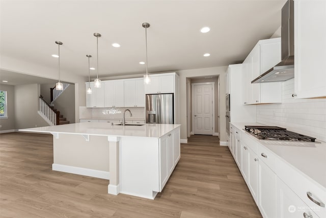 kitchen featuring sink, hanging light fixtures, an island with sink, light hardwood / wood-style floors, and stainless steel appliances