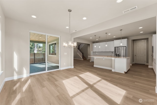 kitchen with stainless steel refrigerator with ice dispenser, a spacious island, decorative light fixtures, light hardwood / wood-style flooring, and white cabinets