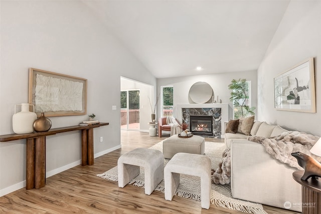 living room with high vaulted ceiling, a high end fireplace, and light wood-type flooring