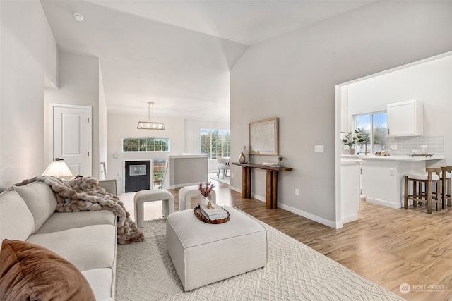 living room with an inviting chandelier, light hardwood / wood-style flooring, and high vaulted ceiling