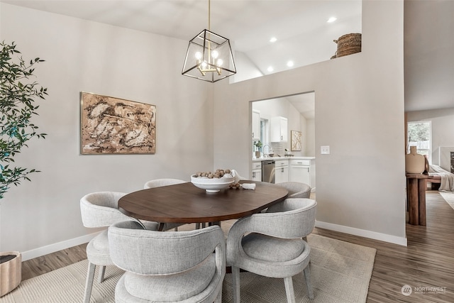 dining area featuring wood-type flooring, a towering ceiling, sink, and an inviting chandelier