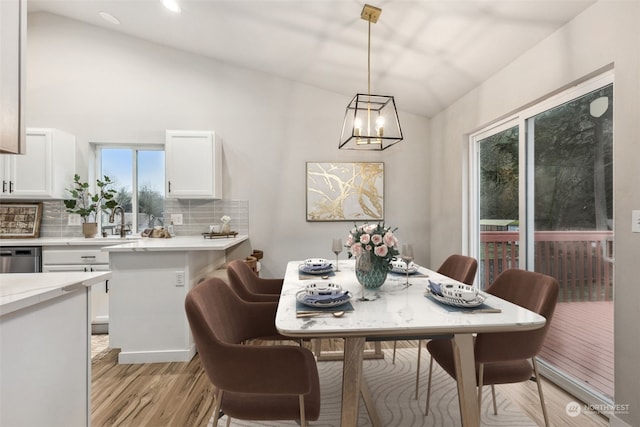 dining space with lofted ceiling, light wood-type flooring, and an inviting chandelier