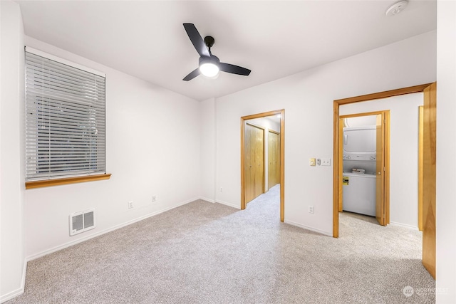 unfurnished bedroom with light carpet, stacked washing maching and dryer, and ceiling fan