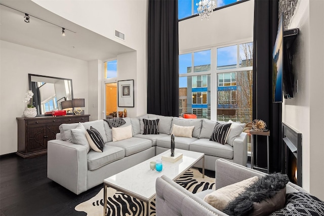 living room with a towering ceiling, rail lighting, a wealth of natural light, and dark wood-type flooring