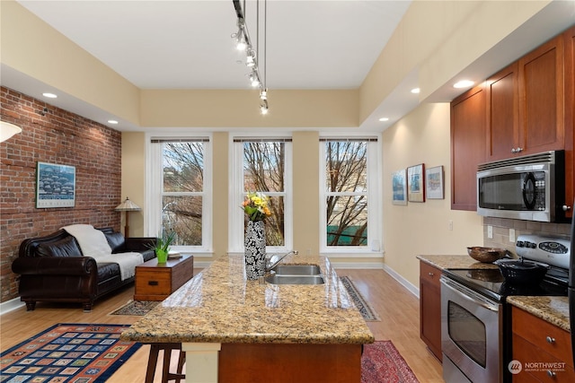 kitchen with light stone countertops, sink, stainless steel appliances, brick wall, and light hardwood / wood-style floors