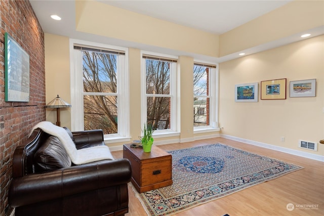 living area with plenty of natural light, wood-type flooring, and brick wall