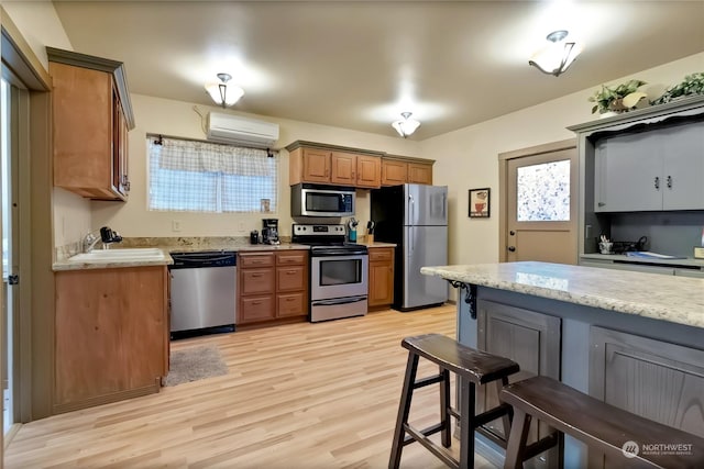 kitchen with stainless steel appliances, sink, a wall unit AC, and light hardwood / wood-style flooring