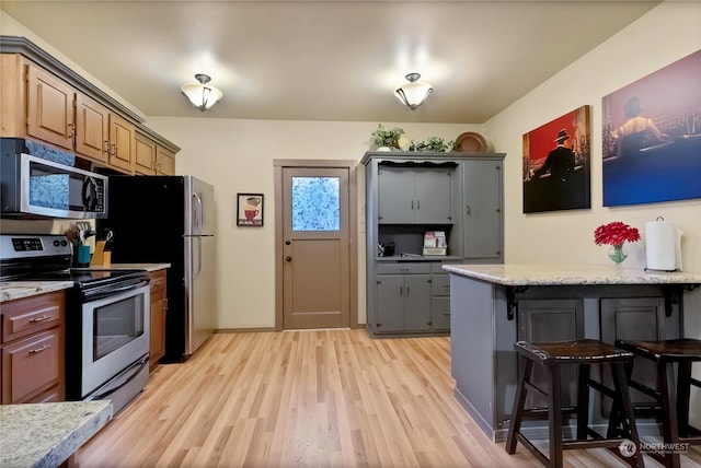 kitchen with light hardwood / wood-style flooring, a breakfast bar area, light stone countertops, and appliances with stainless steel finishes