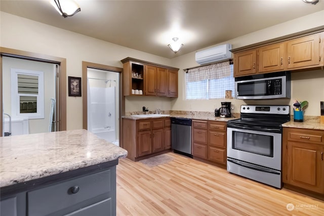 kitchen featuring sink, light hardwood / wood-style flooring, stainless steel appliances, a wall mounted AC, and light stone countertops