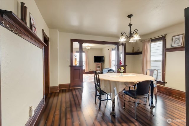 dining space with dark wood-type flooring, a chandelier, and ornate columns